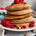 stack of almond pulp pancakes topped with fruit, pecans and chocolate chips