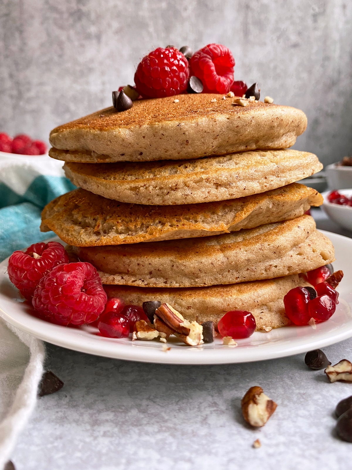 stack of almond pulp pancakes topped with fruit, pecans and chocolate chips