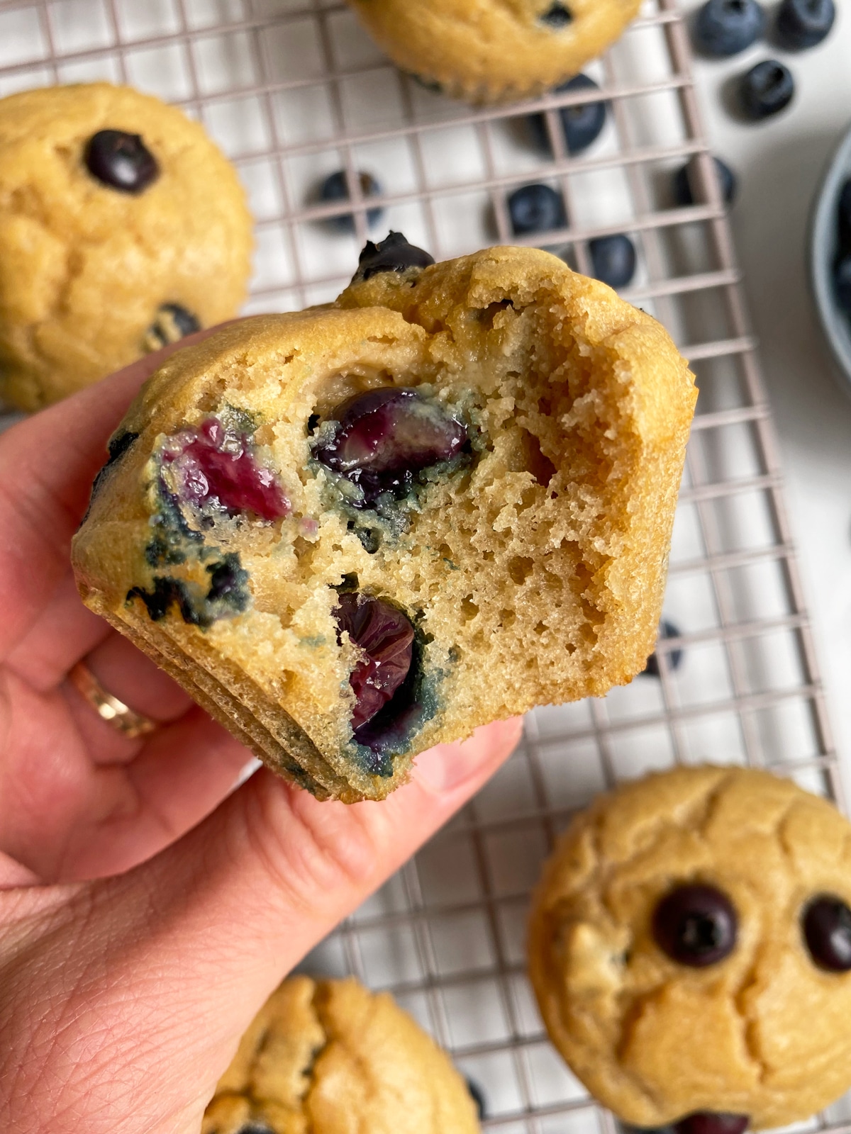 holding a blueberry cassava flour muffin with a bite taken out