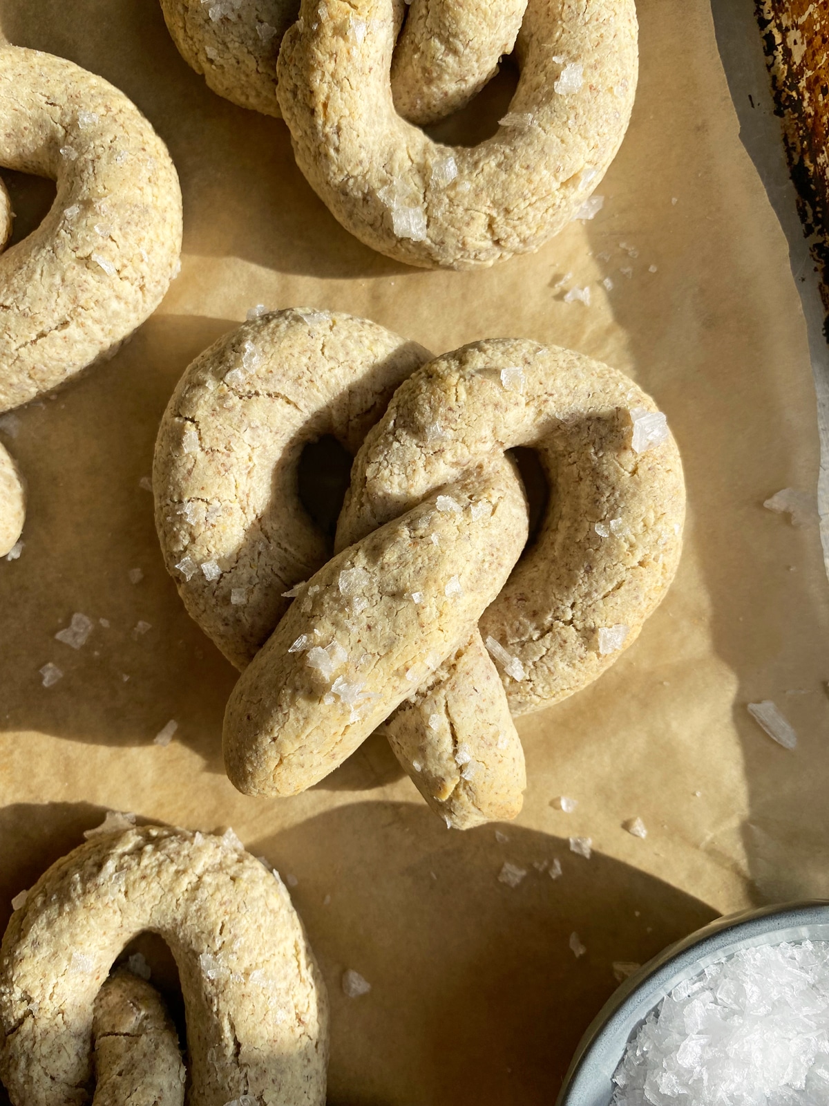 soft baked pretzel on parchment lined baking sheet, sprinkled with flaked salt