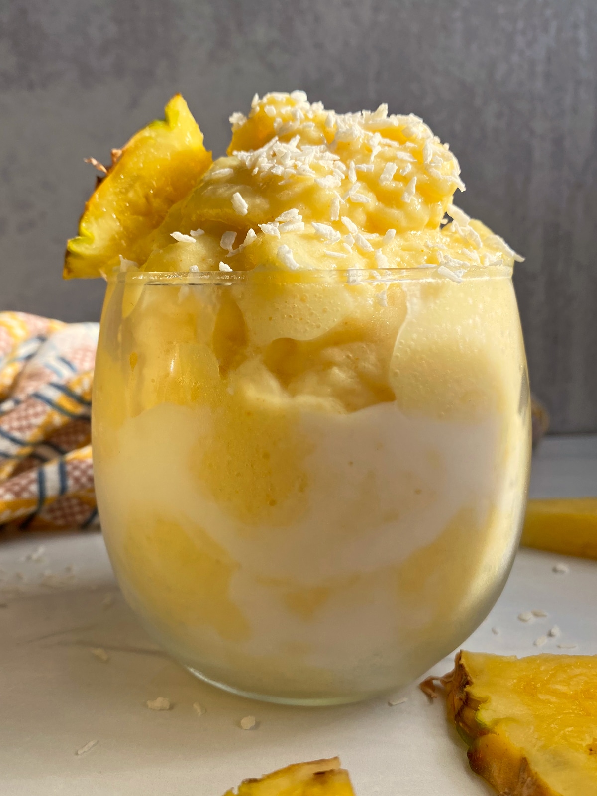 smoothie in a glass cup, topped with shredded coconut and a slice of pineapple