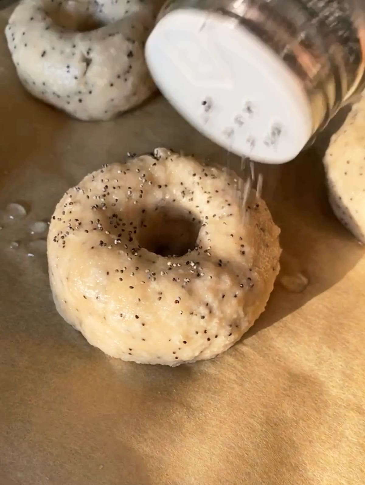 boiled bagels being topped with poppy seeds