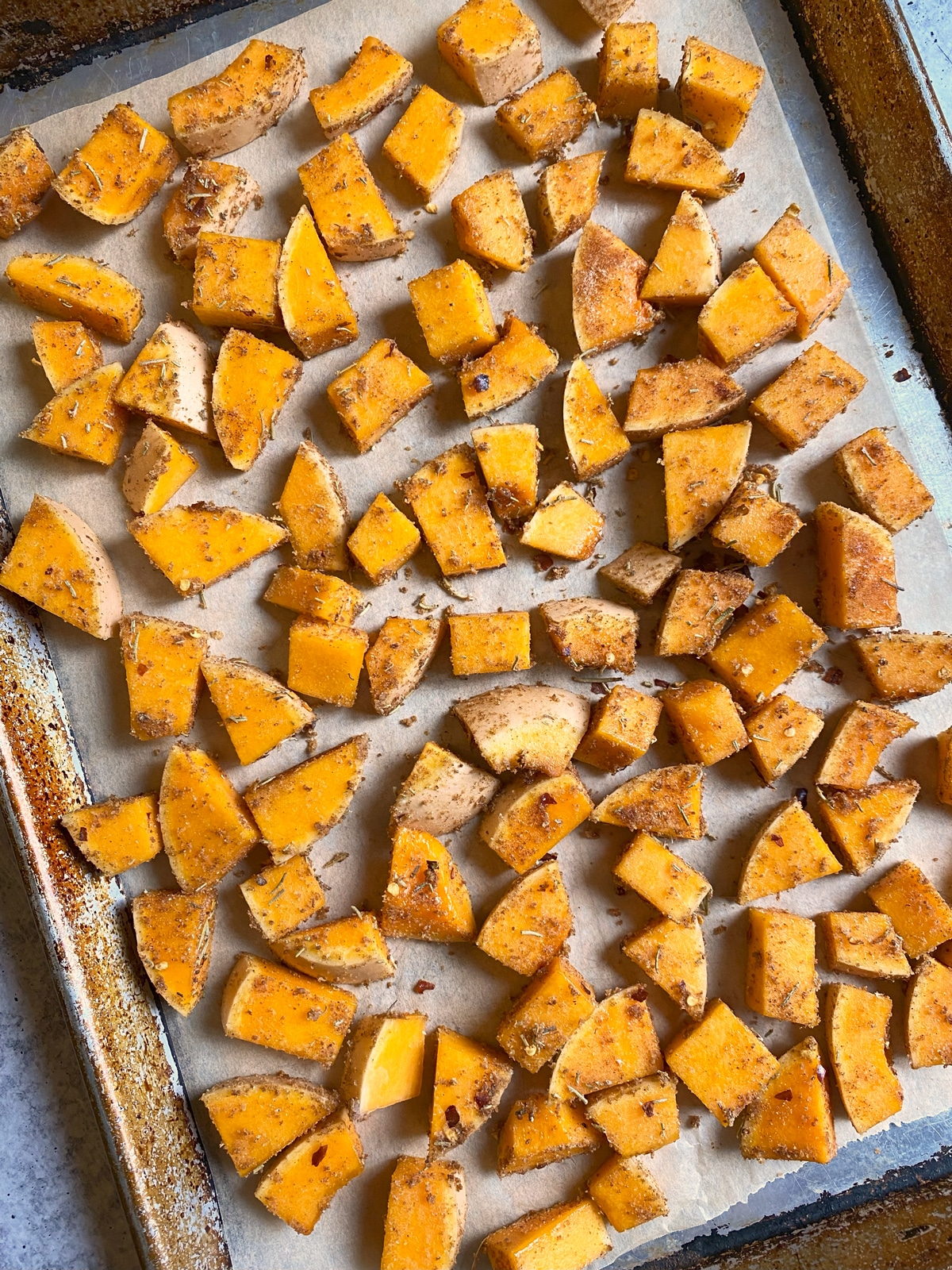 Cut and seasoned squash laid out on a parchment-lined baking sheet.