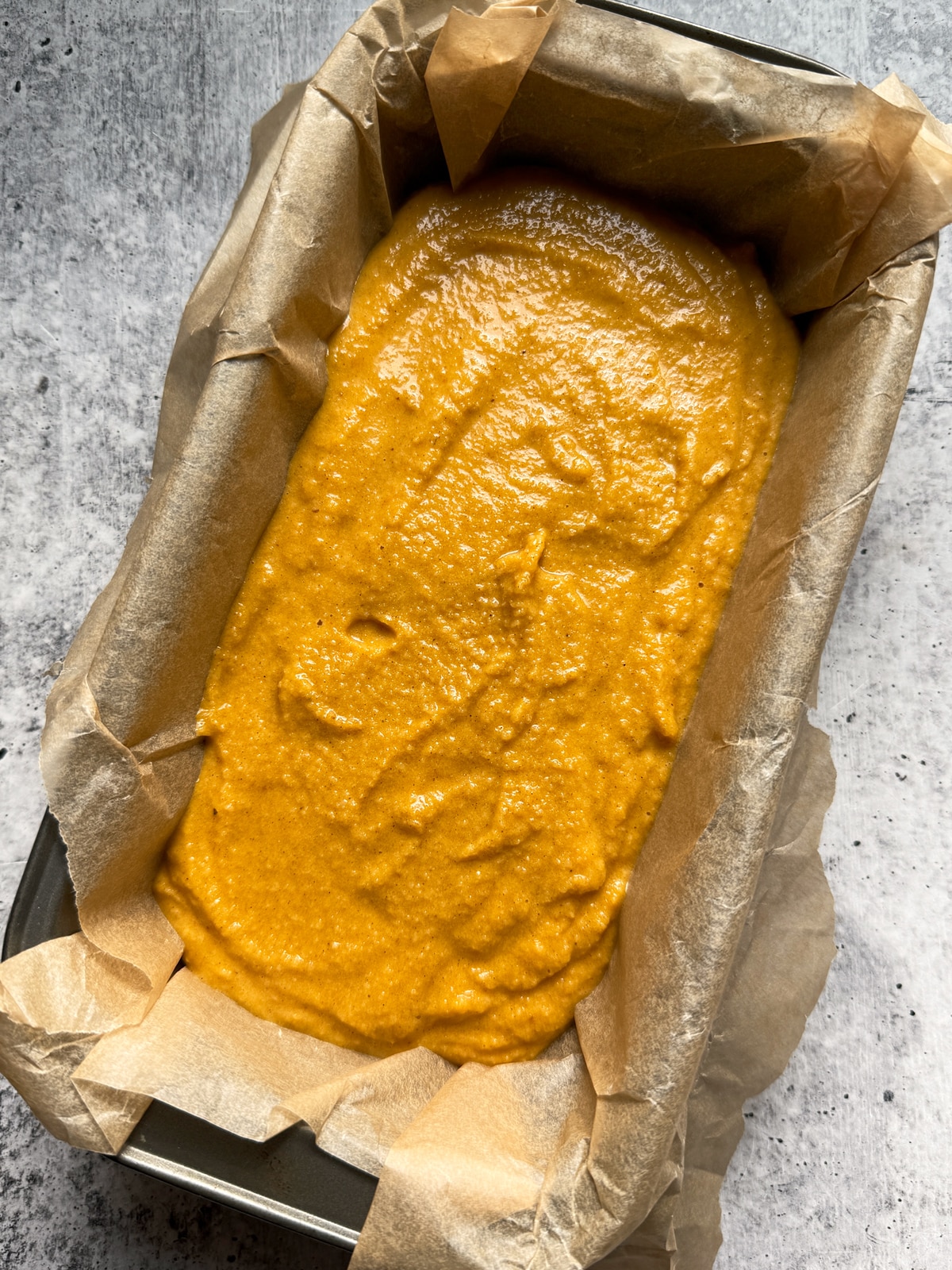 Bread batter in lined loaf pan.