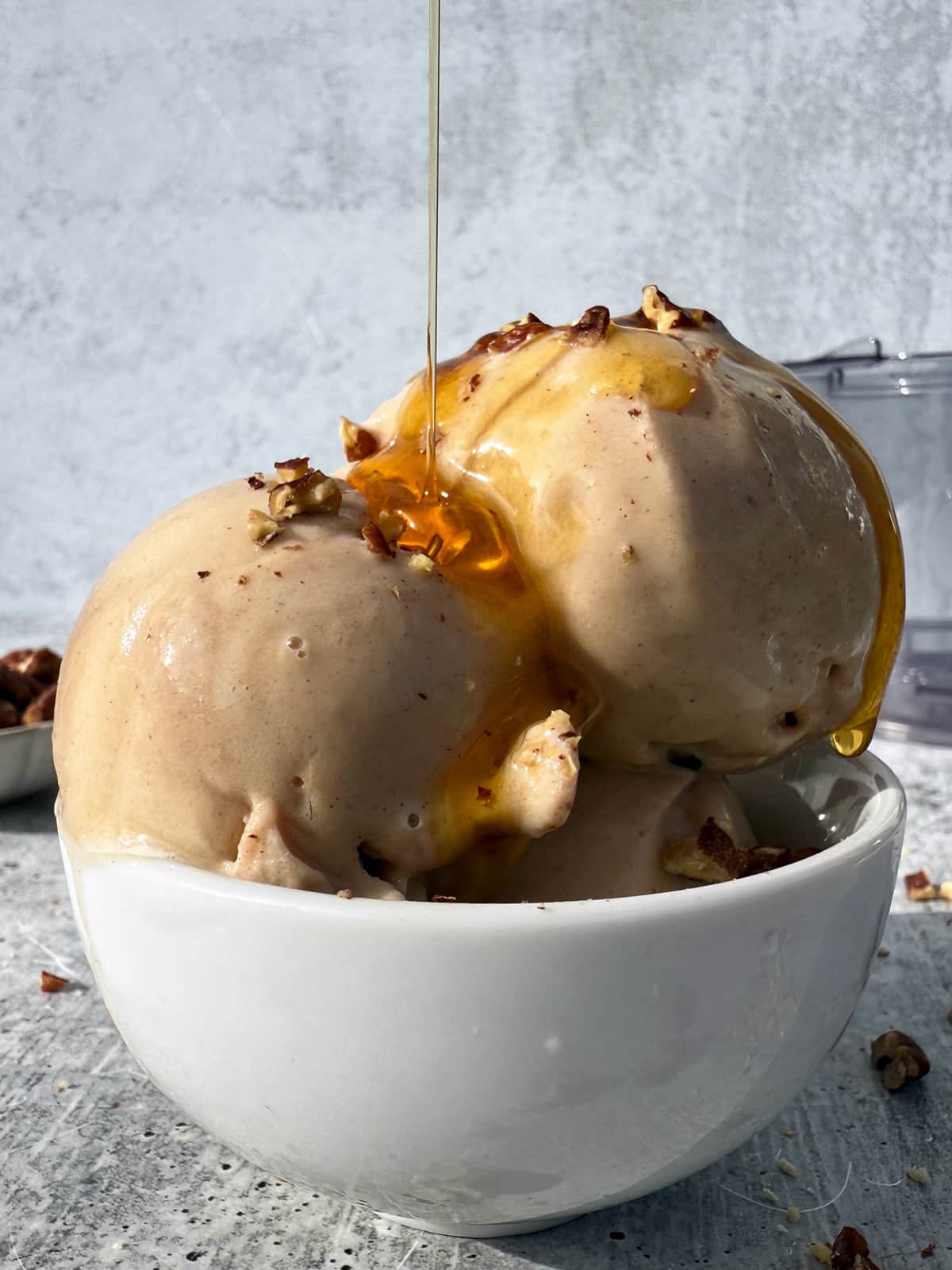 Scooped ice cream topped with maple syrup and crushed pecans.