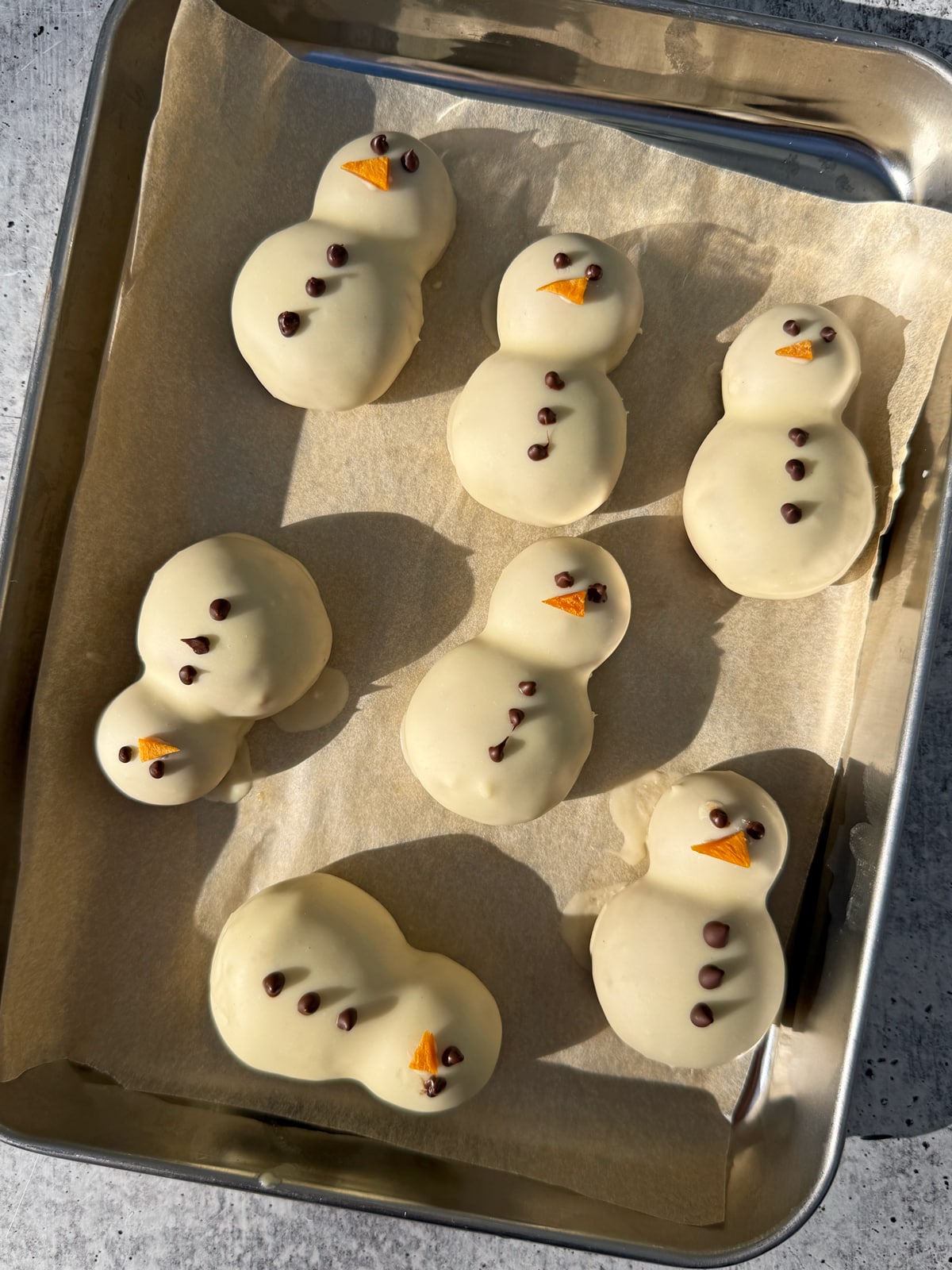Protein balls shaped like snowmen on a lined baking sheet.