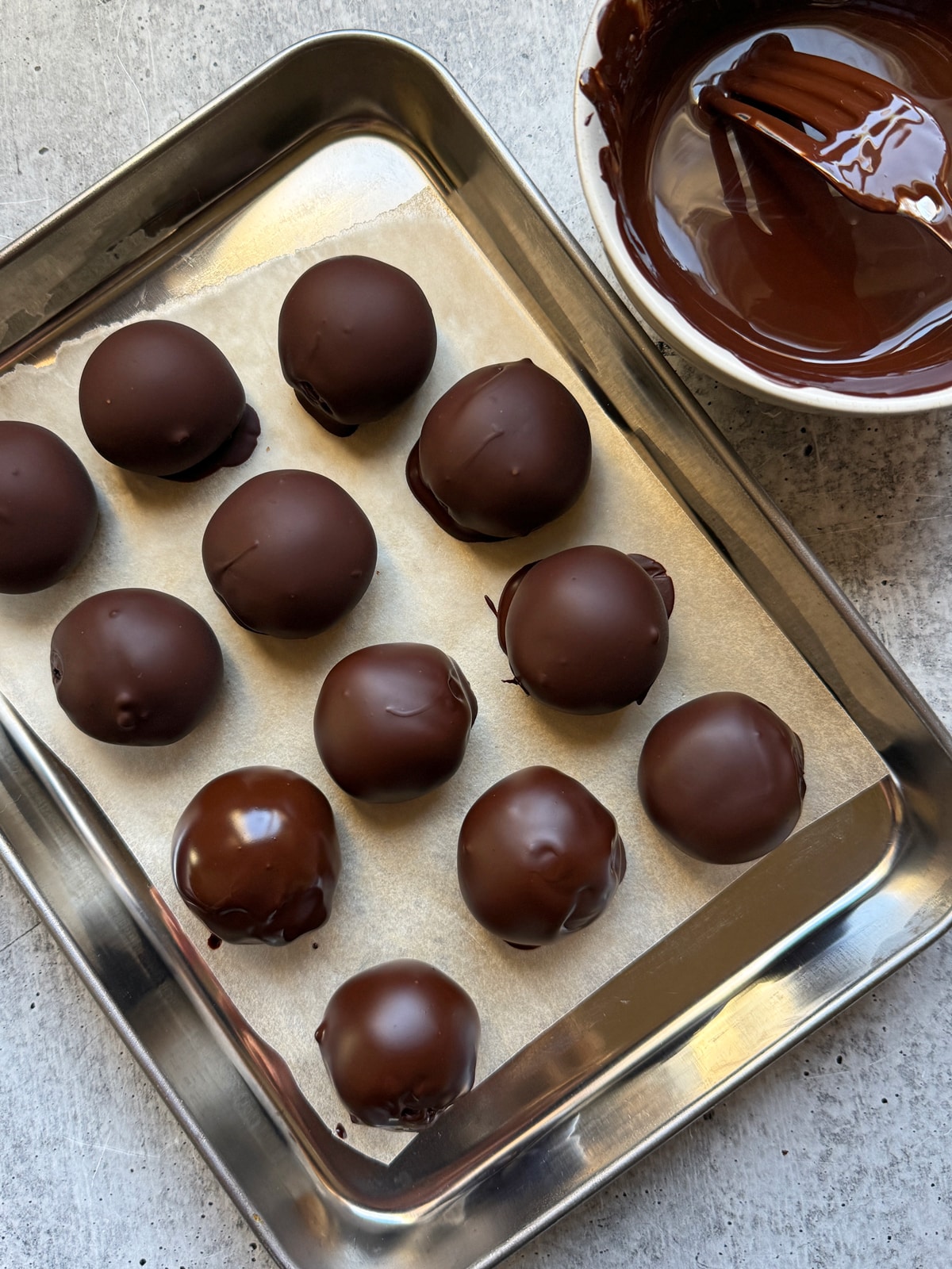 Fillings dipped in dark chocolate and drying on lined baking sheet.