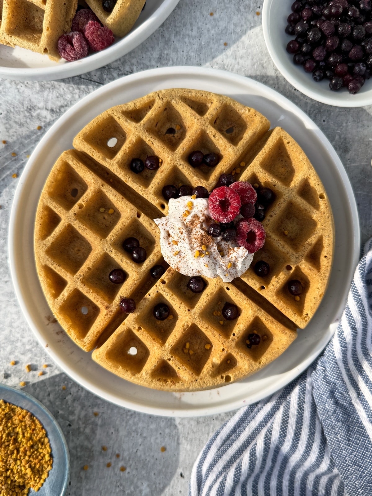 Plated waffle topped with coconut cream, frozen berries and bee pollen.