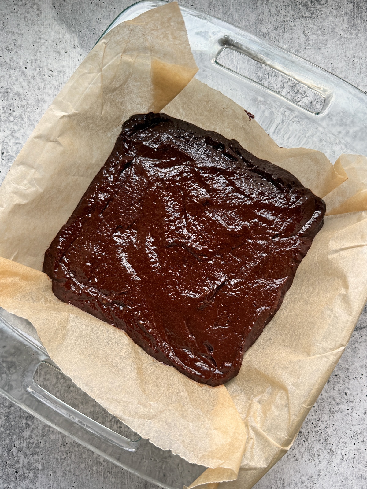 Brownie batter in lined baking dish, ready to bake.