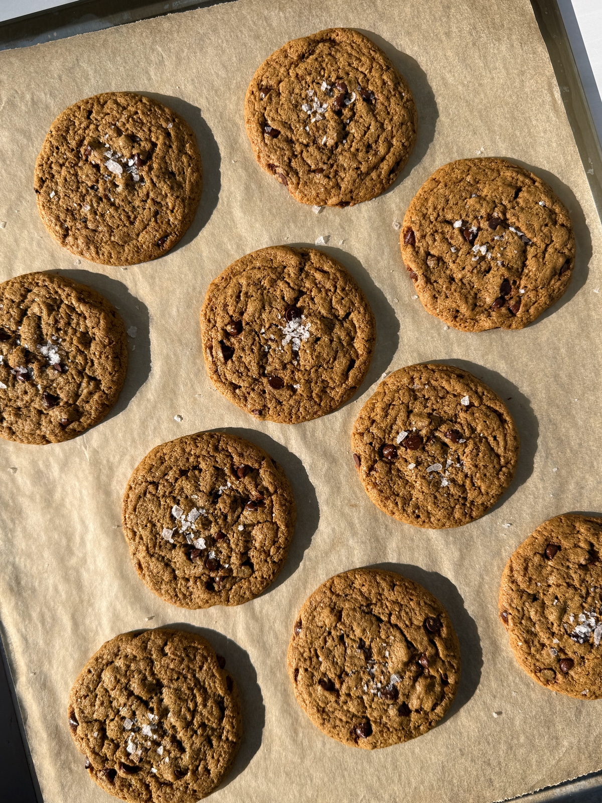 Freshly baked cookies on lined baking sheet, topped with flaked salt.