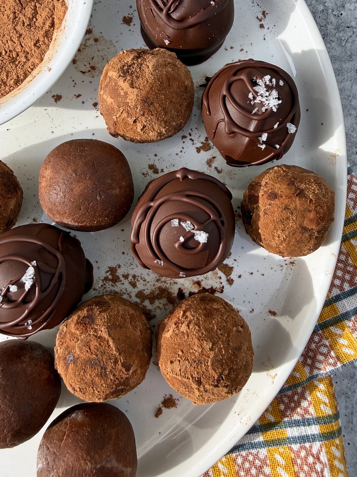 Sunbutter protein balls on a plate. Some plain, some rolled in cacao powder and some dipped in dark chocolate.