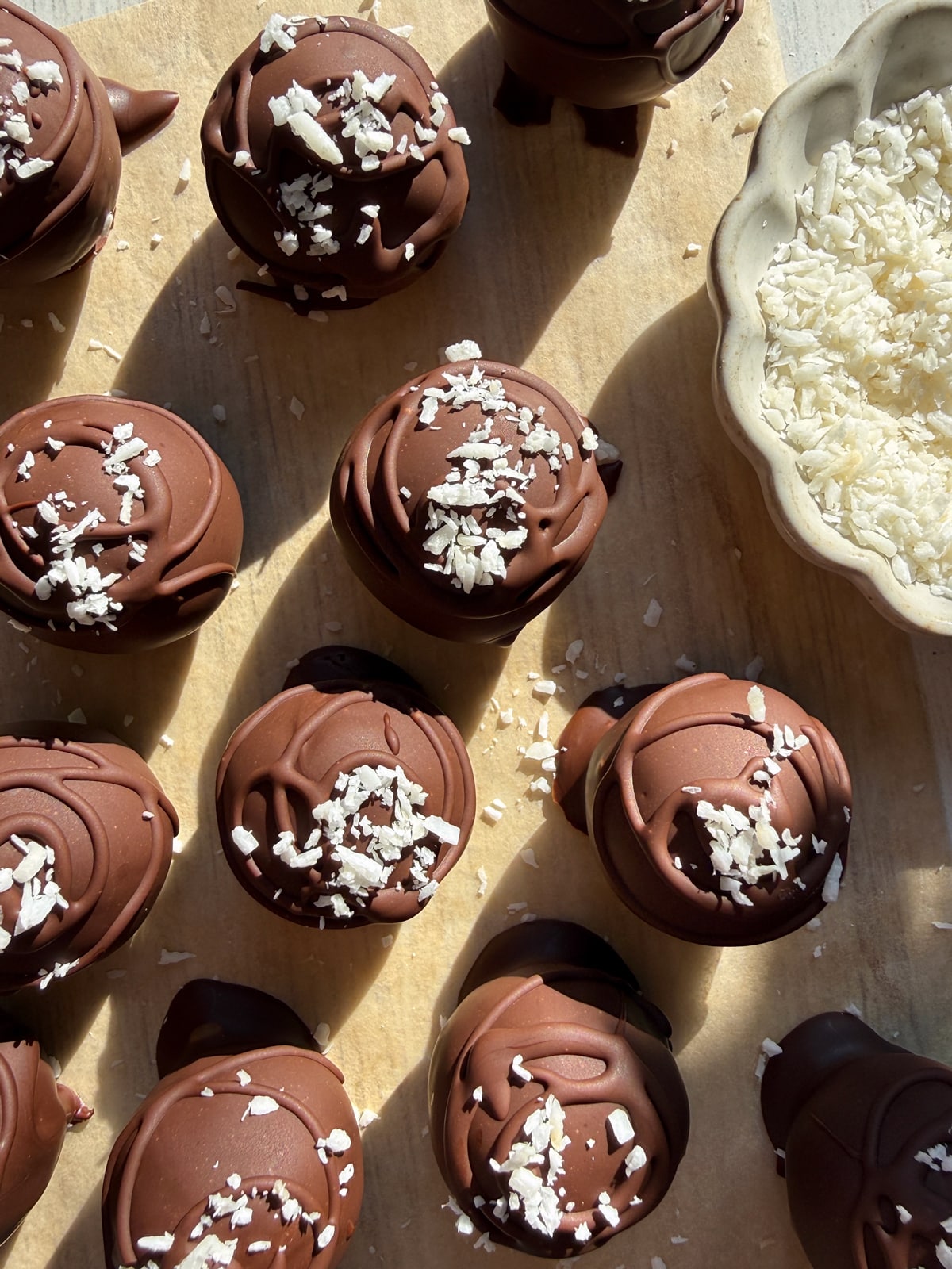 Coconut and date balls dipped in dark chocolate and topped with shredded coconut.