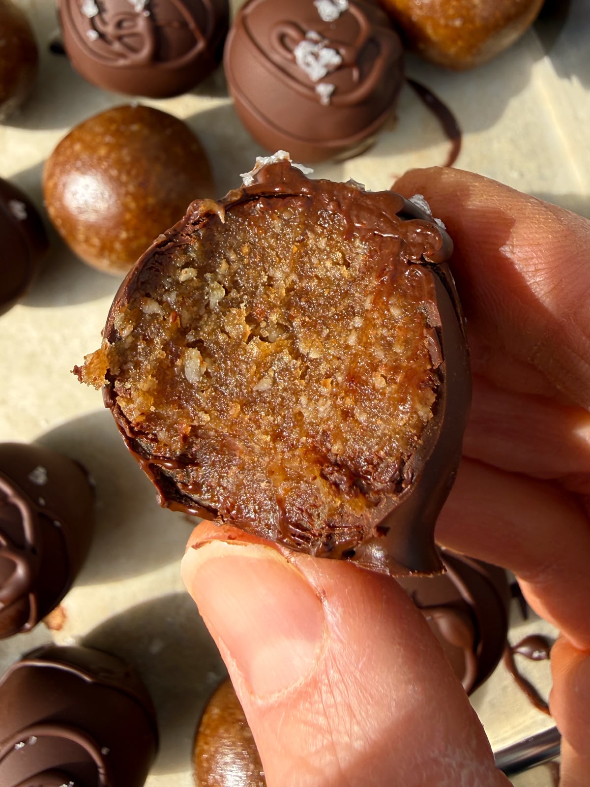 Holding an almond date ball with a bite out of it.