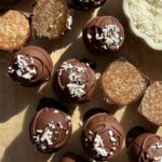 Coconut date balls dipped in chocolate and topped with shredded coconut.