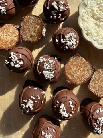 Coconut date balls dipped in chocolate and topped with shredded coconut.