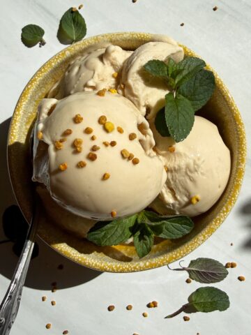 Bowl of ice cream topped with mint leaves and bee pollen.