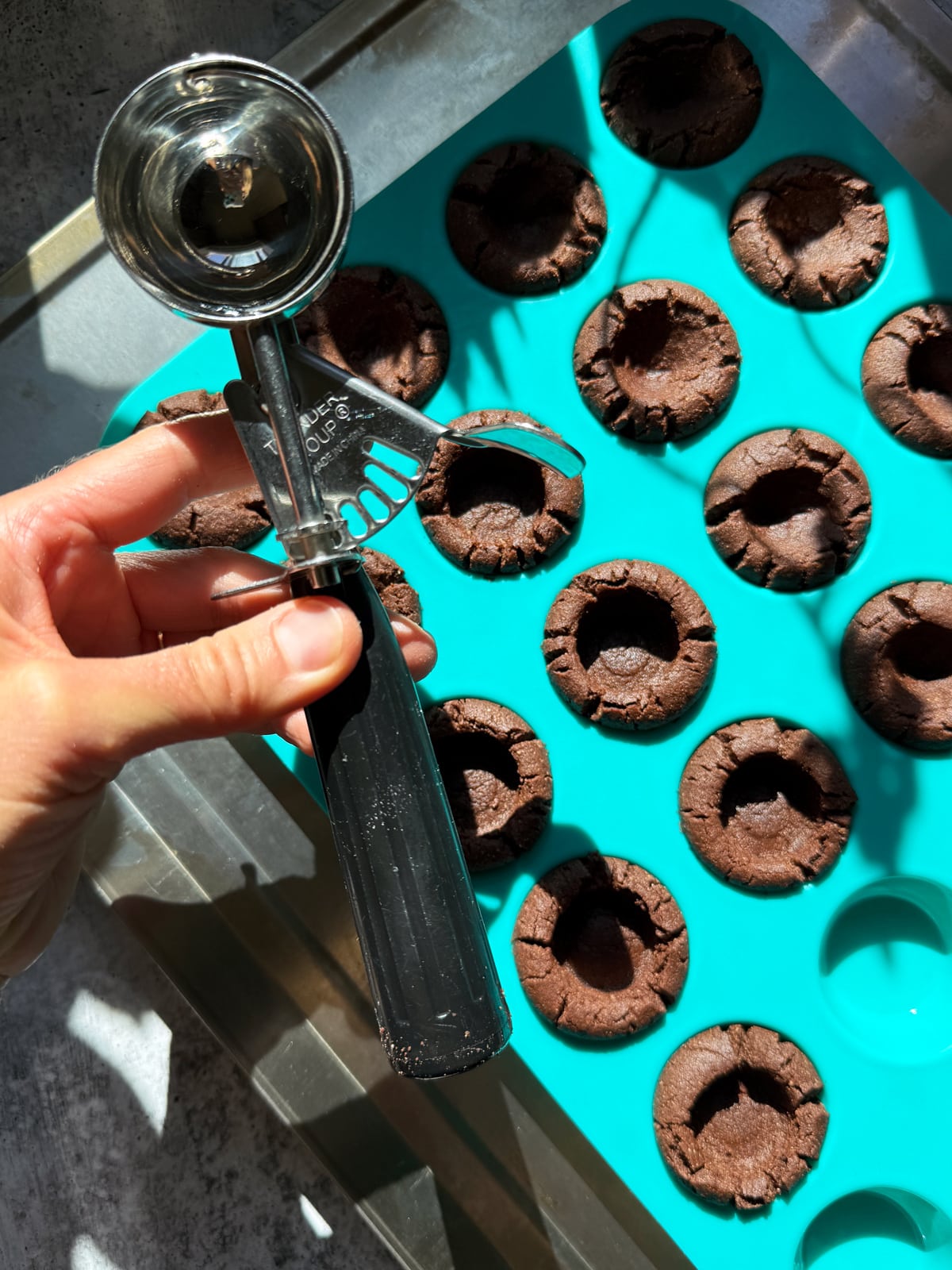 Using the end of a large cookie scoop to make indentations in the baked cookie cups.