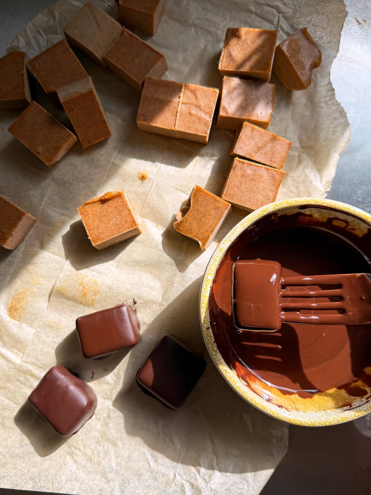 Dipping the frozen and cut caramel in the dark chocolate.