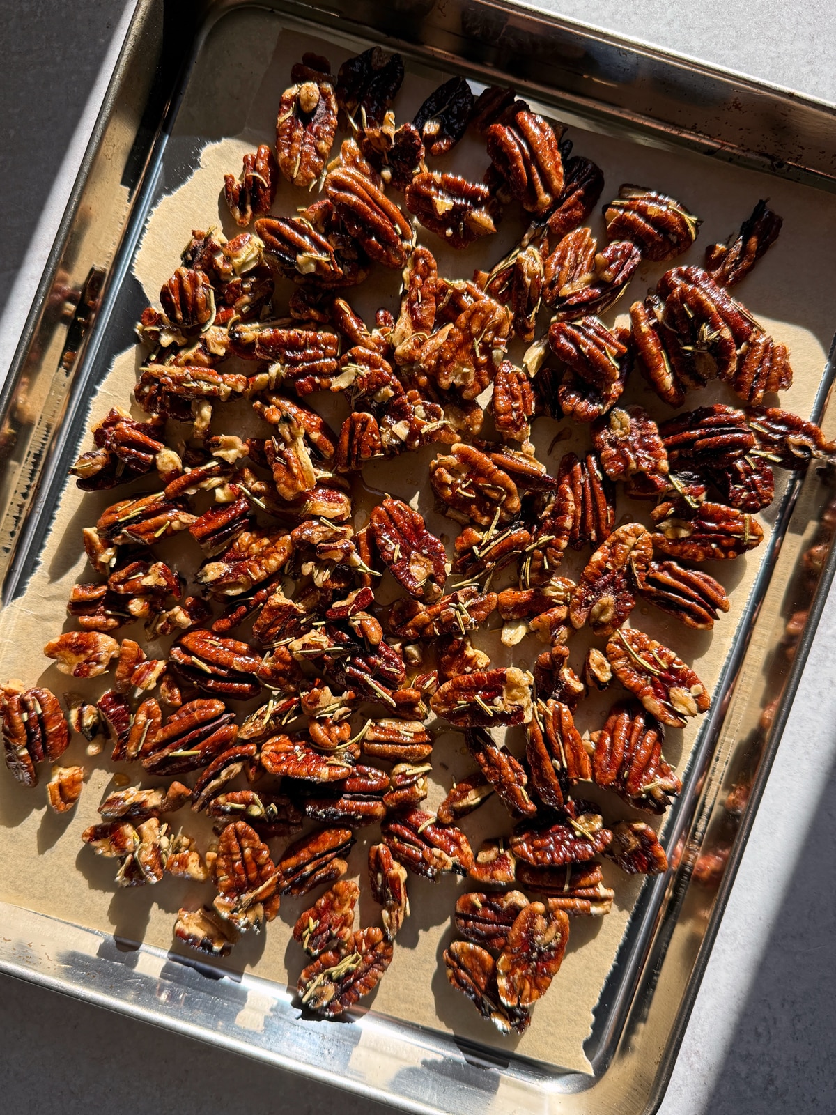 Maple rosemary pecans on a lined baking sheet, ready to bake.